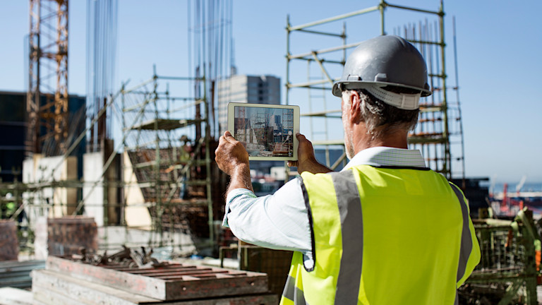 Man holding up a tablet taking a picture of the construction site