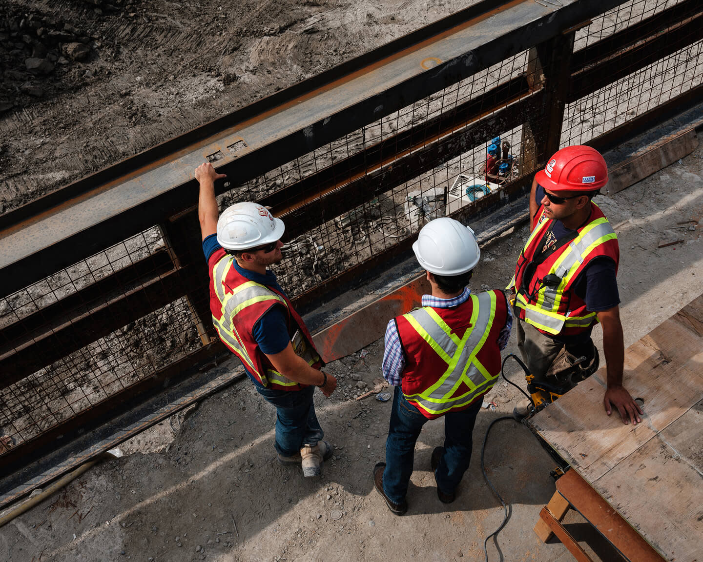 Three construction workers in safety vests and helmets discussing at site.